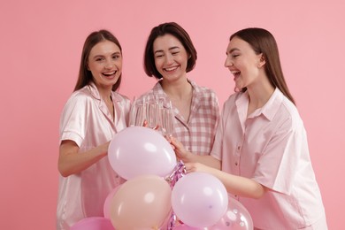 Photo of Pajama party. Happy friends with balloons clinking glasses on pink background