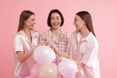 Photo of Pajama party. Happy friends with balloons clinking glasses on pink background