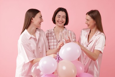 Photo of Pajama party. Happy friends with balloons clinking glasses on pink background