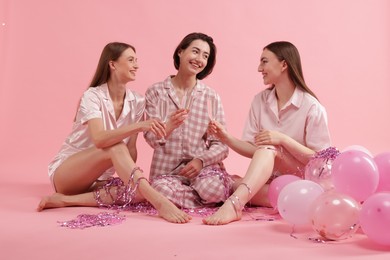 Photo of Pajama party. Happy friends with balloons and tinsel clinking glasses on pink background