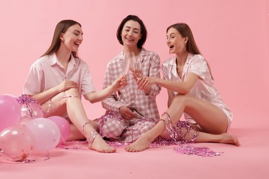 Photo of Pajama party. Happy friends with balloons and tinsel clinking glasses on pink background