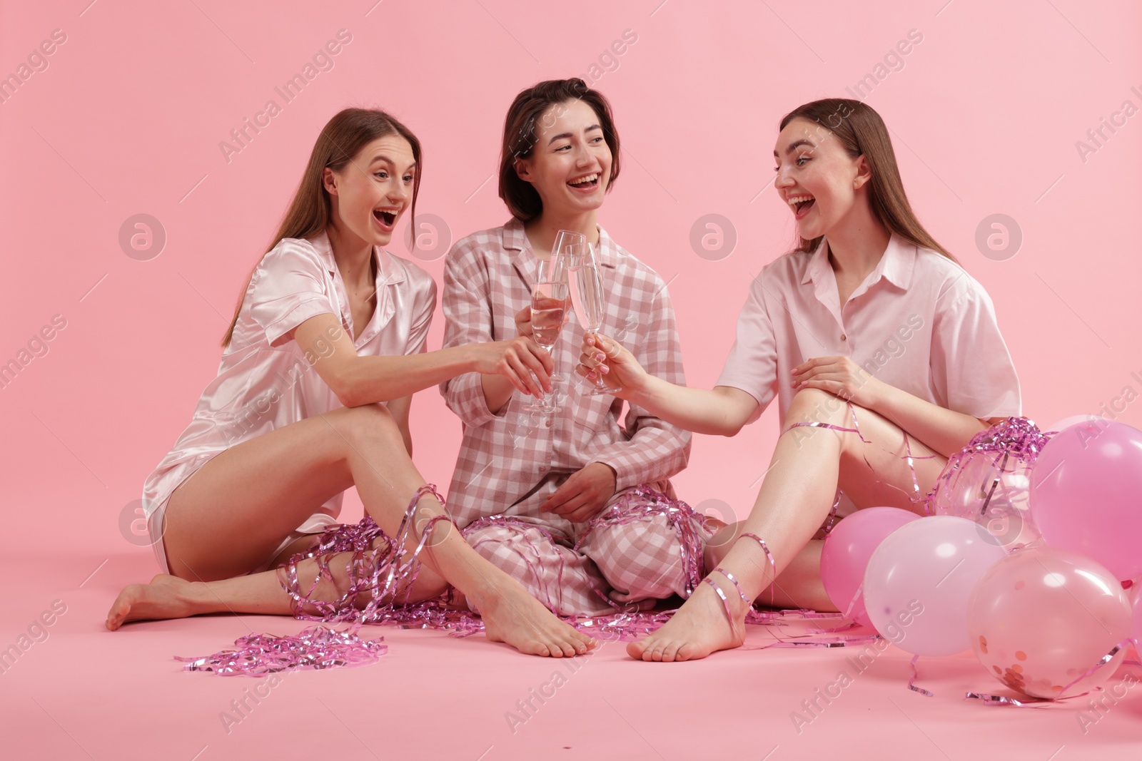 Photo of Pajama party. Happy friends with balloons and tinsel clinking glasses on pink background