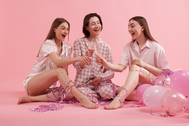 Photo of Pajama party. Happy friends with balloons and tinsel clinking glasses on pink background