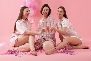 Photo of Pajama party. Happy friends with balloons and tinsel clinking glasses on pink background