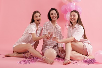 Photo of Pajama party. Happy friends with balloons and tinsel clinking glasses on pink background
