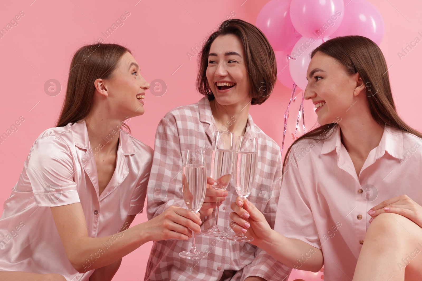 Photo of Pajama party. Happy friends clinking glasses on pink background
