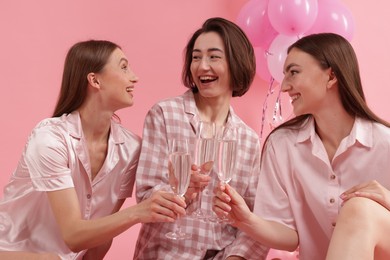Photo of Pajama party. Happy friends clinking glasses on pink background