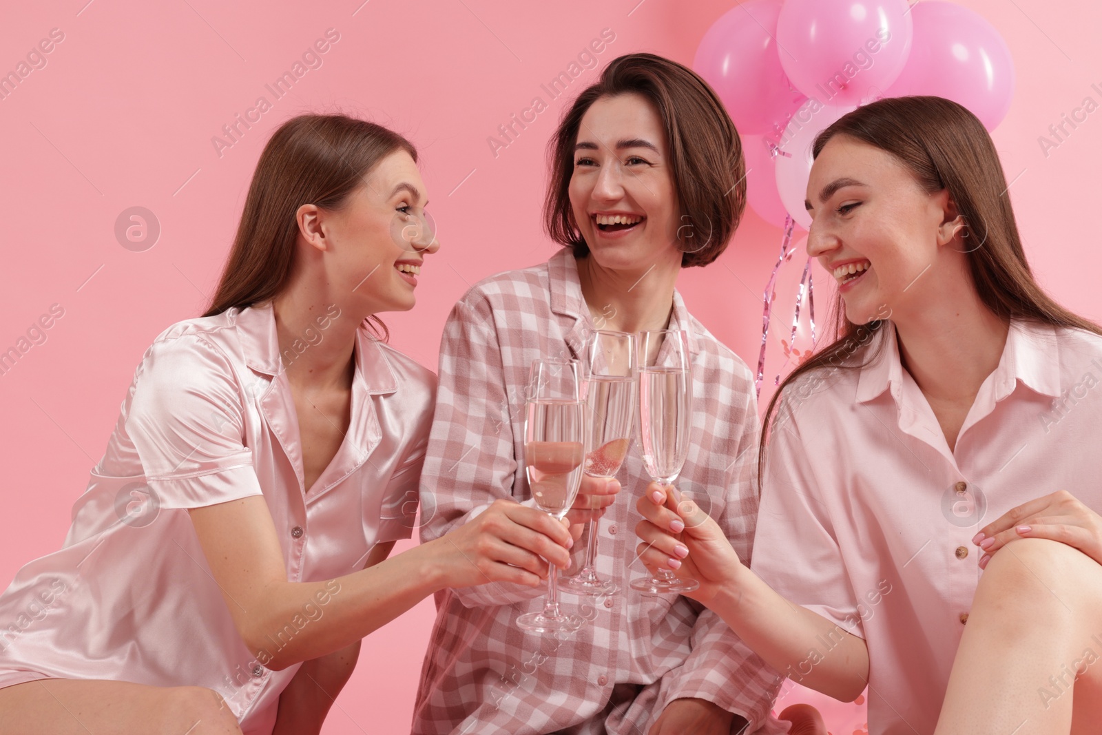 Photo of Pajama party. Happy friends clinking glasses on pink background