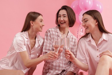 Photo of Pajama party. Happy friends clinking glasses on pink background
