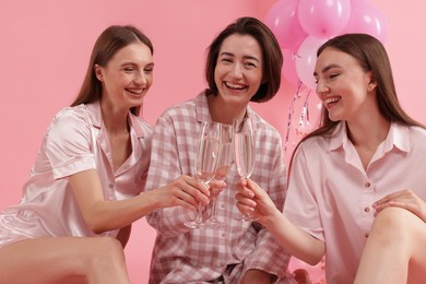 Photo of Pajama party. Happy friends clinking glasses on pink background