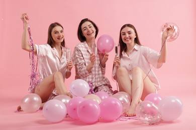 Photo of Pajama party. Happy friends with glasses, balloons and tinsel on pink background