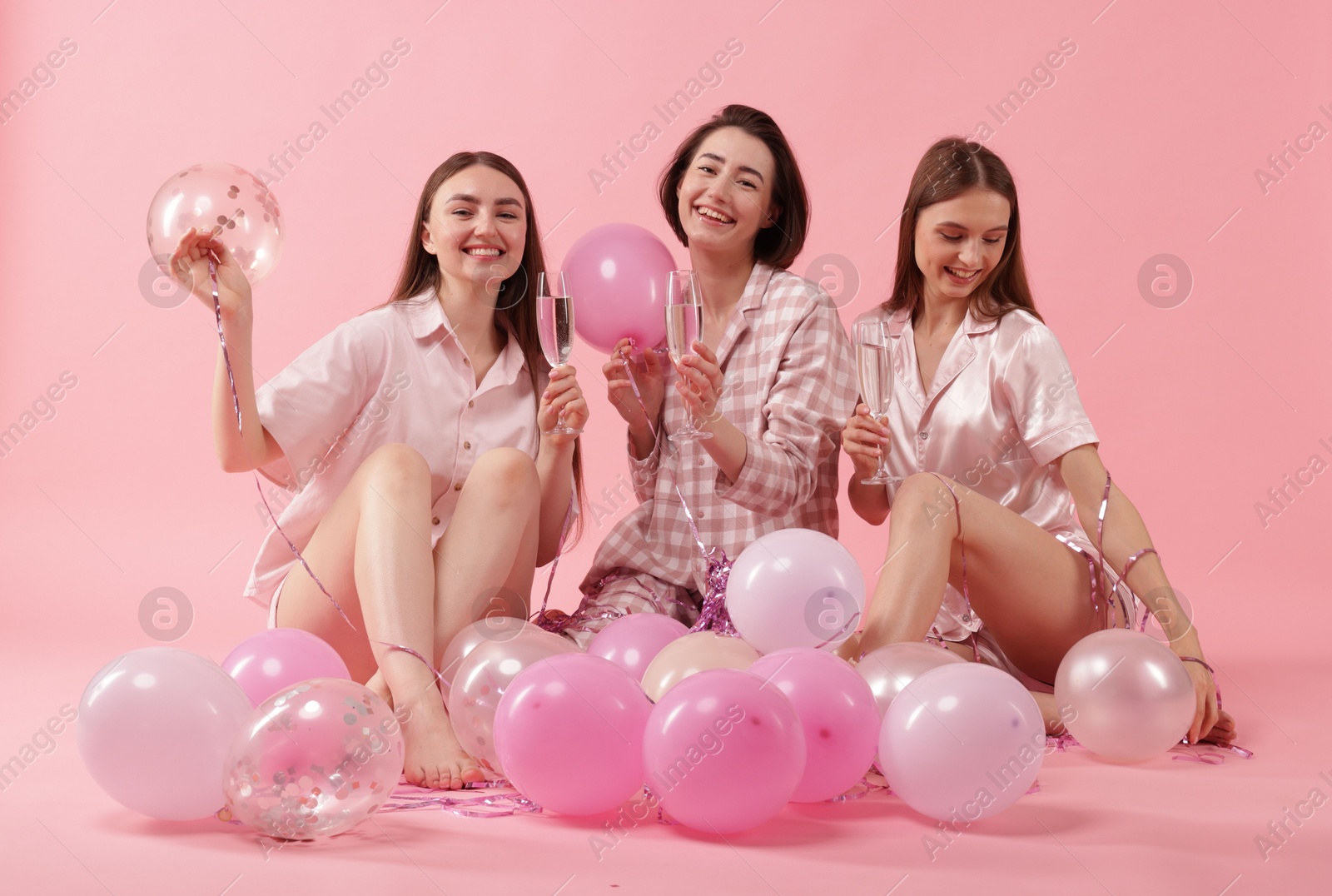Photo of Pajama party. Happy friends with glasses, balloons and tinsel on pink background