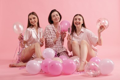Photo of Pajama party. Happy friends with glasses, balloons and tinsel on pink background