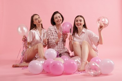 Photo of Pajama party. Happy friends with glasses, balloons and tinsel on pink background