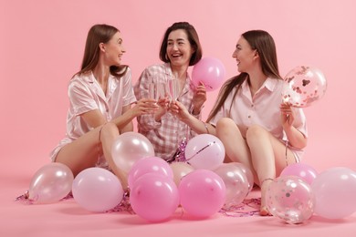 Photo of Pajama party. Happy friends with balloons and tinsel clinking glasses on pink background