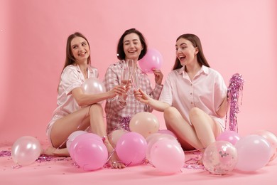 Photo of Pajama party. Happy friends with balloons and tinsel clinking glasses on pink background