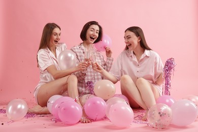 Photo of Pajama party. Happy friends with balloons and tinsel clinking glasses on pink background