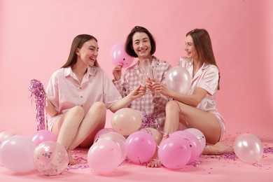 Photo of Pajama party. Happy friends with balloons and tinsel clinking glasses on pink background