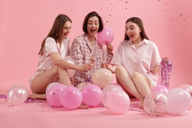 Photo of Pajama party. Happy friends with balloons and tinsel clinking glasses under falling confetti on pink background