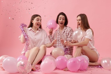 Photo of Pajama party. Happy friends with balloons and tinsel clinking glasses under falling confetti on pink background