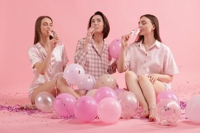 Photo of Pajama party. Happy friends with glasses, balloons and tinsel on pink background