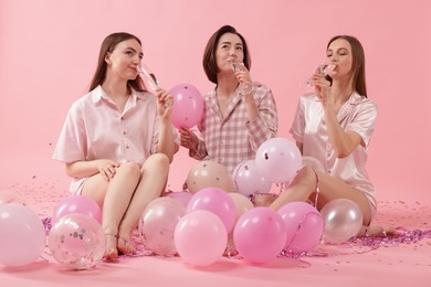Photo of Pajama party. Happy friends with glasses, balloons and tinsel on pink background