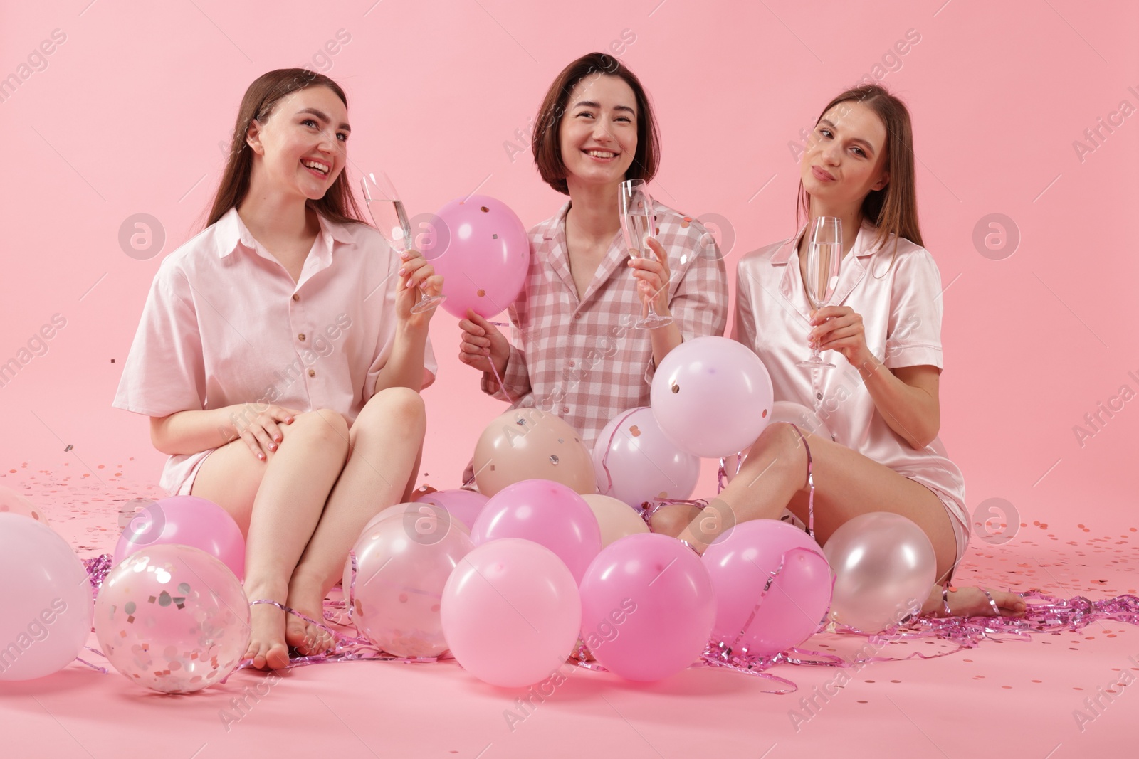 Photo of Pajama party. Happy friends with glasses, balloons and tinsel on pink background
