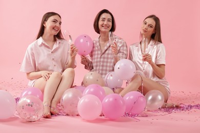 Photo of Pajama party. Happy friends with glasses, balloons and tinsel on pink background