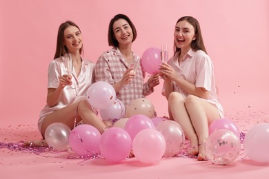 Photo of Pajama party. Happy friends with glasses, balloons and tinsel on pink background