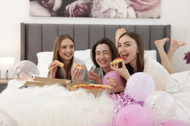 Photo of Pajama party. Happy friends eating pizza on bed at home