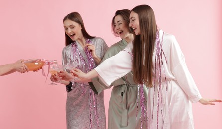 Photo of Pajama day. Woman pouring alcoholic drink for her happy friends on pink background, closeup