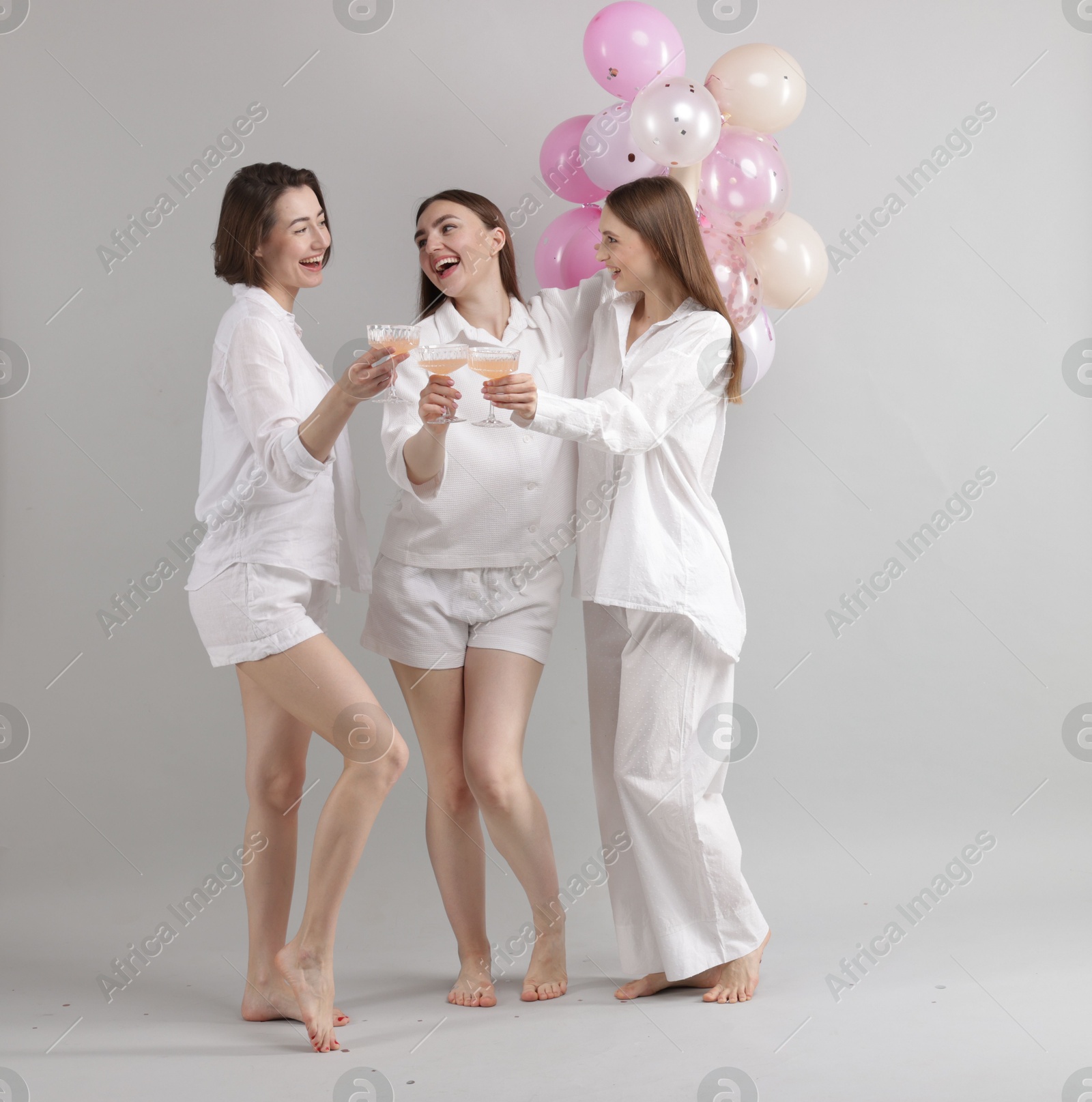 Photo of Pajama party. Happy friends with balloons clinking glasses on grey background