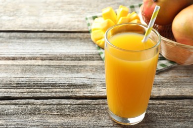 Photo of Tasty mango juice in glass and fresh fruits on wooden table, closeup. Space for text