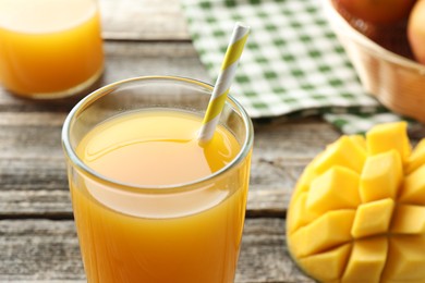 Photo of Tasty mango juice in glass and fresh fruit on wooden table, closeup