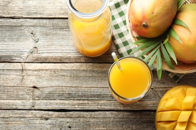 Photo of Tasty mango juice in glass, carafe, fresh fruits and leaves on wooden table, flat lay. Space for text