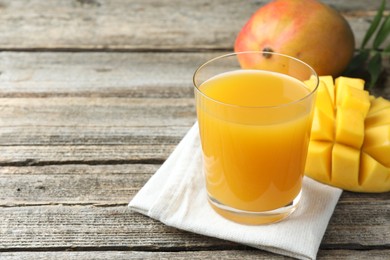 Photo of Tasty mango juice in glass, fresh fruits and green leaves on wooden table, closeup. Space for text