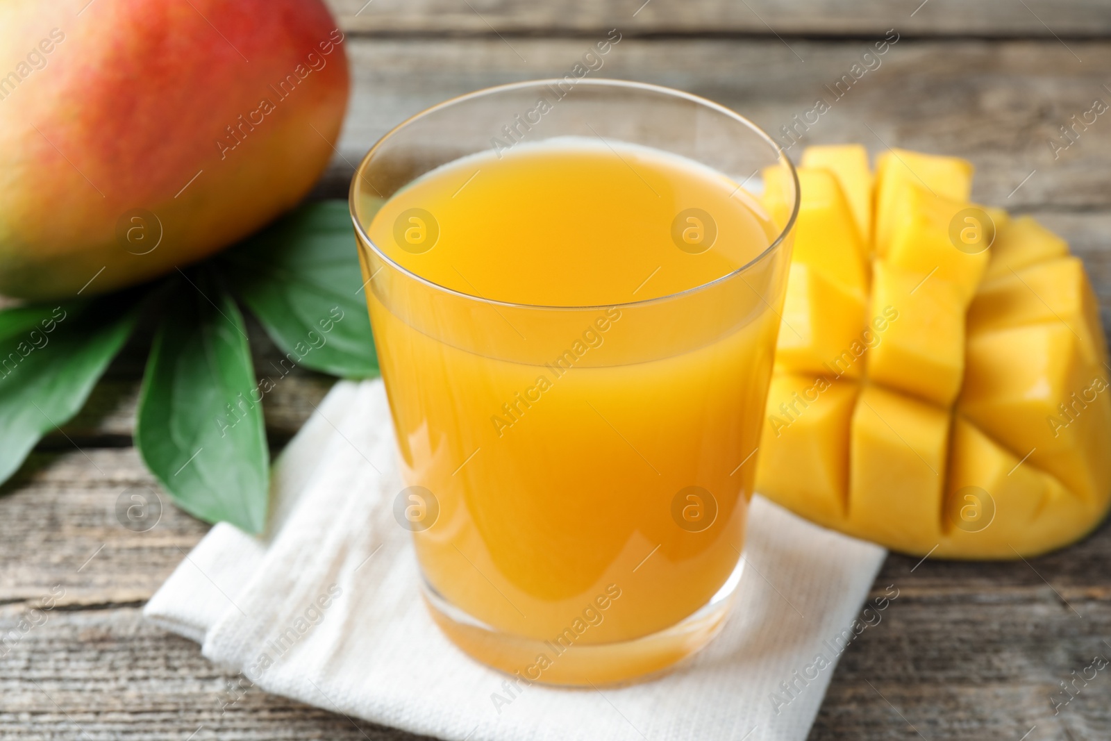 Tasty mango juice in glass, fresh fruits and green leaves on wooden table, closeup Photo of Tasty mango juice in glass, fresh fruits and green leaves on wooden table, closeup