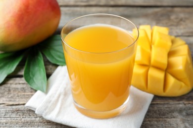 Photo of Tasty mango juice in glass, fresh fruits and green leaves on wooden table, closeup