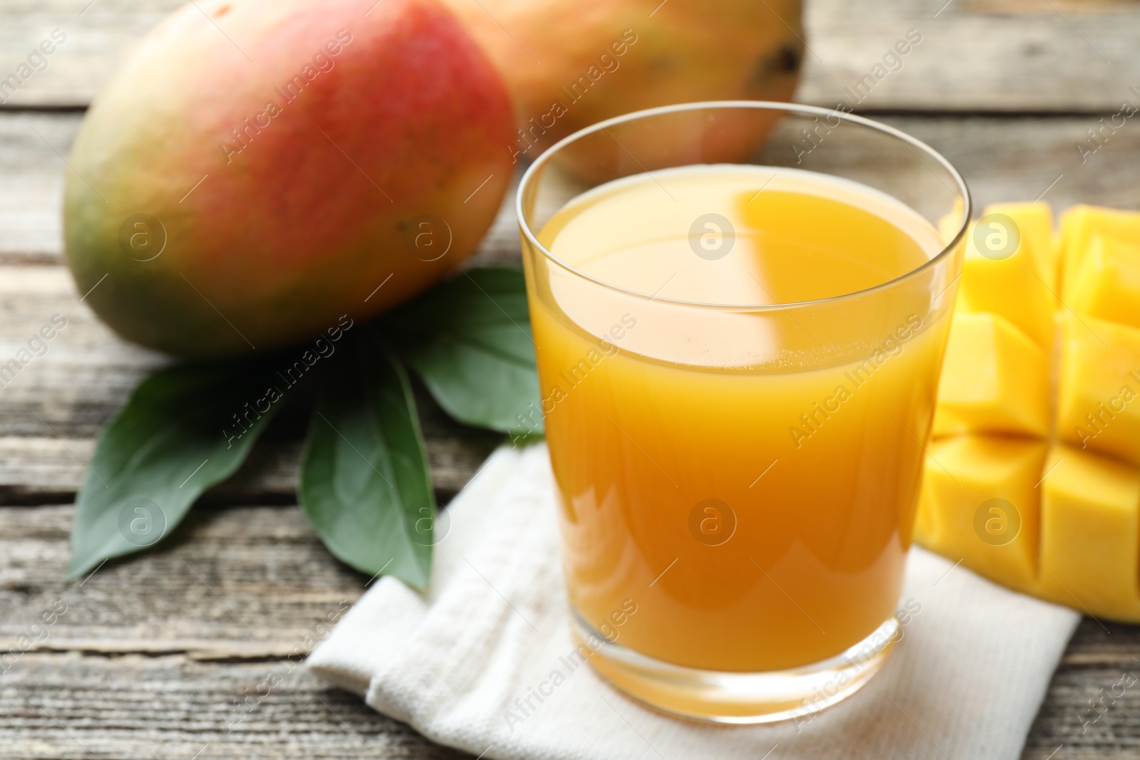 Tasty mango juice in glass, fresh fruits and green leaves on wooden table, closeup Photo of Tasty mango juice in glass, fresh fruits and green leaves on wooden table, closeup