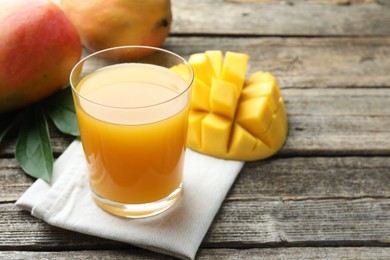 Photo of Tasty mango juice in glass, fresh fruits and green leaves on wooden table, closeup. Space for text