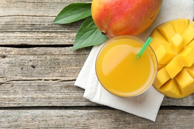 Photo of Tasty mango juice in glass, fresh fruits and leaves on wooden table, flat lay. Space for text