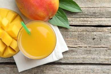 Photo of Tasty mango juice in glass, fresh fruits and leaves on wooden table, flat lay. Space for text