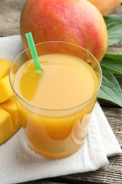 Photo of Tasty mango juice in glass, fresh fruits and green leaves on wooden table, closeup