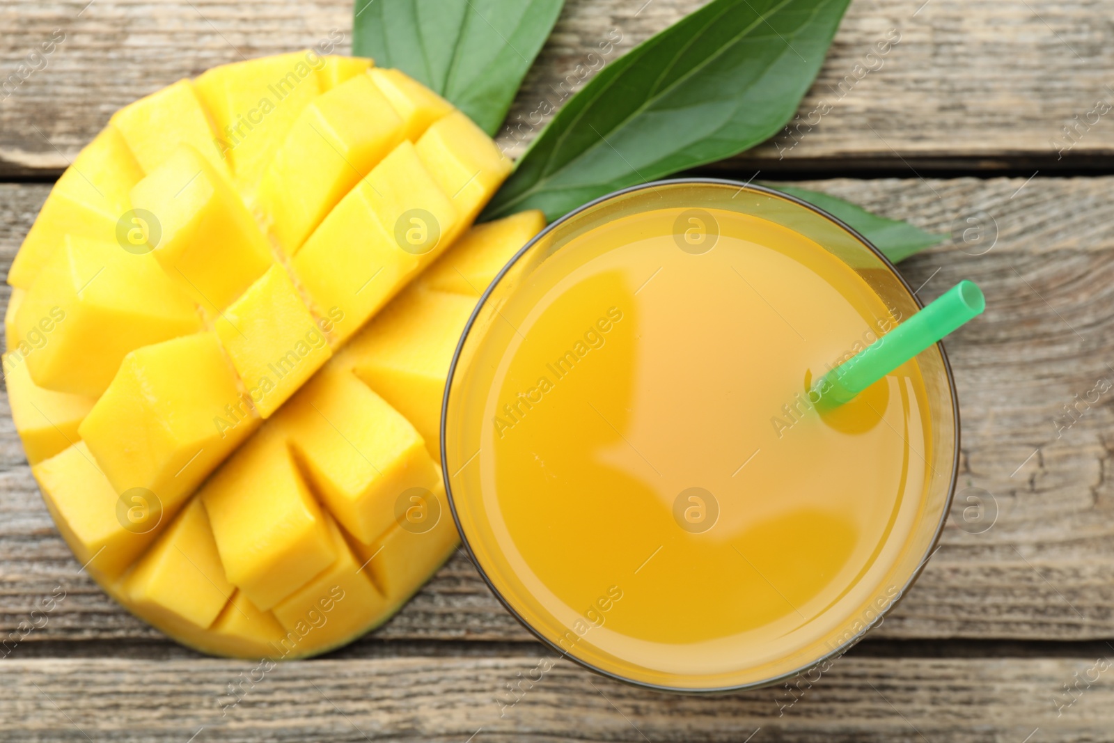 Tasty mango juice in glass, fresh fruit and green leaves on wooden table, flat lay Photo of Tasty mango juice in glass, fresh fruit and green leaves on wooden table, flat lay