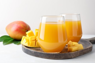 Photo of Tasty mango juice in glasses, fresh fruits and green leaves on white table, closeup