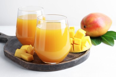 Photo of Tasty mango juice in glasses, fresh fruits and green leaves on white table, closeup