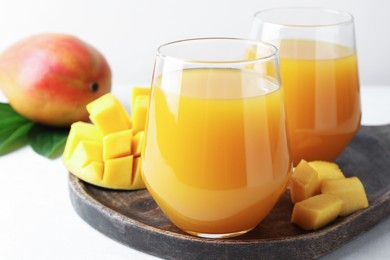 Photo of Tasty mango juice in glasses, fresh fruits and green leaves on white table, closeup