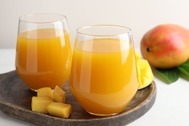 Photo of Tasty mango juice in glasses, fresh fruits and green leaves on white table, closeup