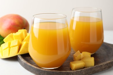 Photo of Tasty mango juice in glasses and fresh fruits on white table, closeup