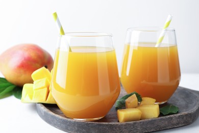Photo of Tasty mango juice in glasses and fresh fruits on white table, closeup